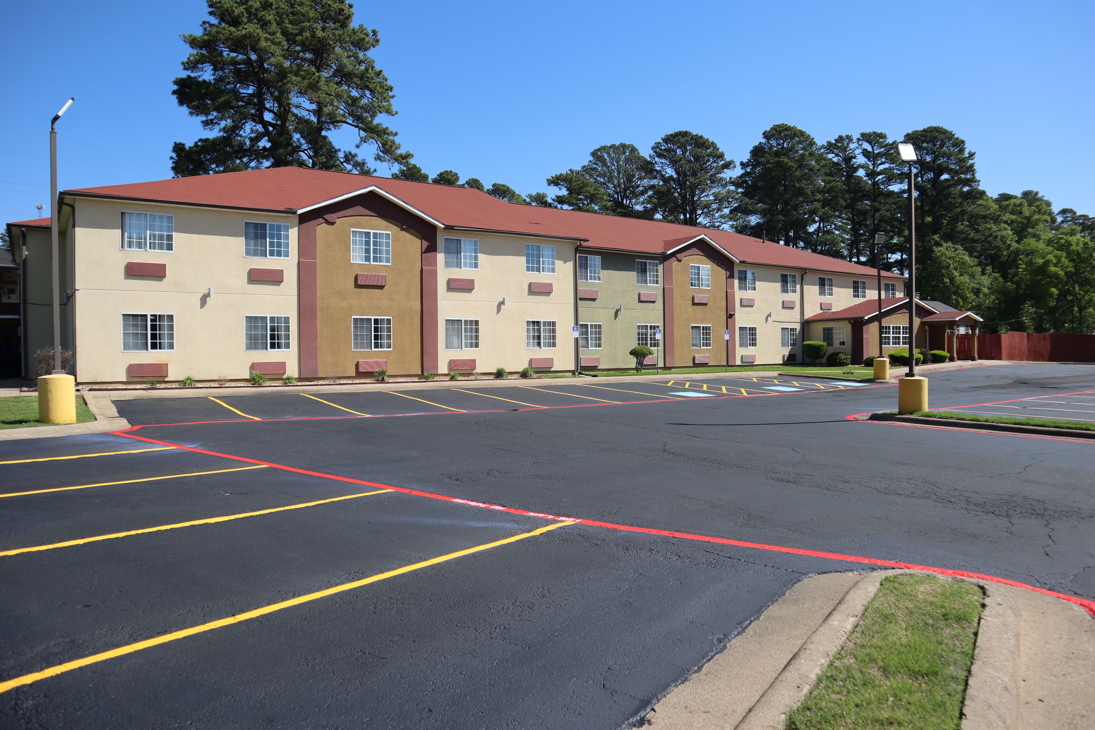A multi-story hotel with a red roof and beige walls, featuring a parking lot with marked spaces.