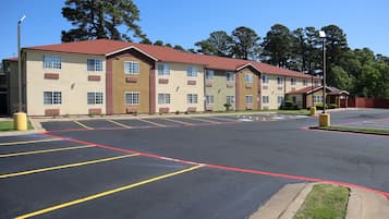 A multi-story hotel with a red roof and beige walls, featuring a parking lot with marked spaces.