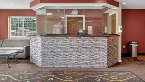 A reception desk with a stone facade, a clock, and a window with a view of houses. - HomeTown Inn & Suites (Longview)