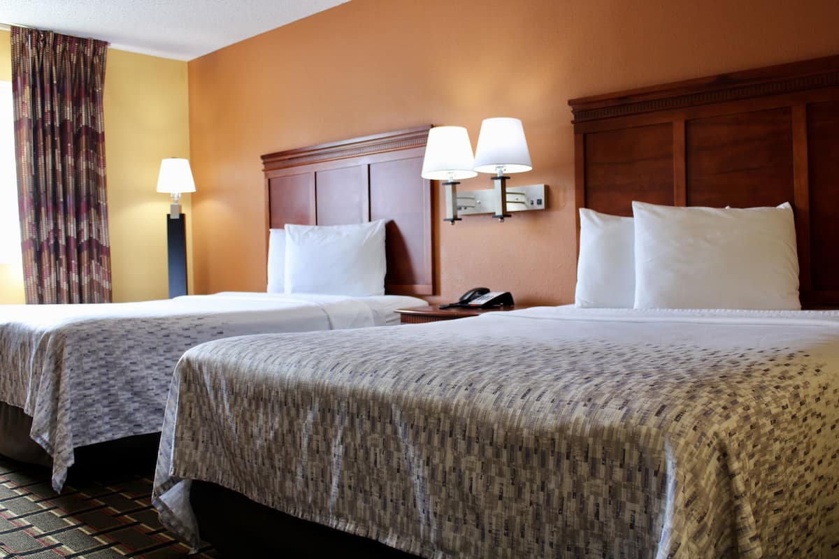 A hotel room with two beds, a nightstand, a telephone, and a wall-mounted lamp.