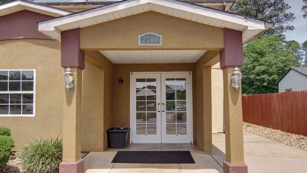 A building with a beige exterior, a double door entrance, and a number sign above the door. - HomeTown Inn & Suites (Longview)