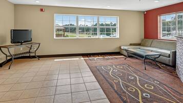 A hotel room with a large window, a flat-screen TV, a sofa, and a patterned rug.