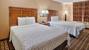 A hotel room with two beds, a nightstand with a phone, wall-mounted lamps, and a patterned carpet. - HomeTown Inn & Suites (Longview)