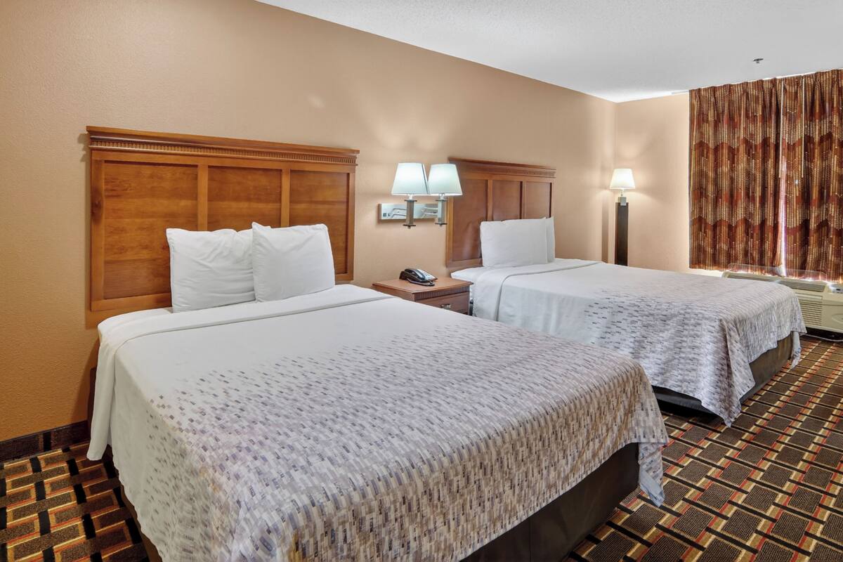 A hotel room with two beds, a nightstand with a phone, wall-mounted lamps, and a patterned carpet.