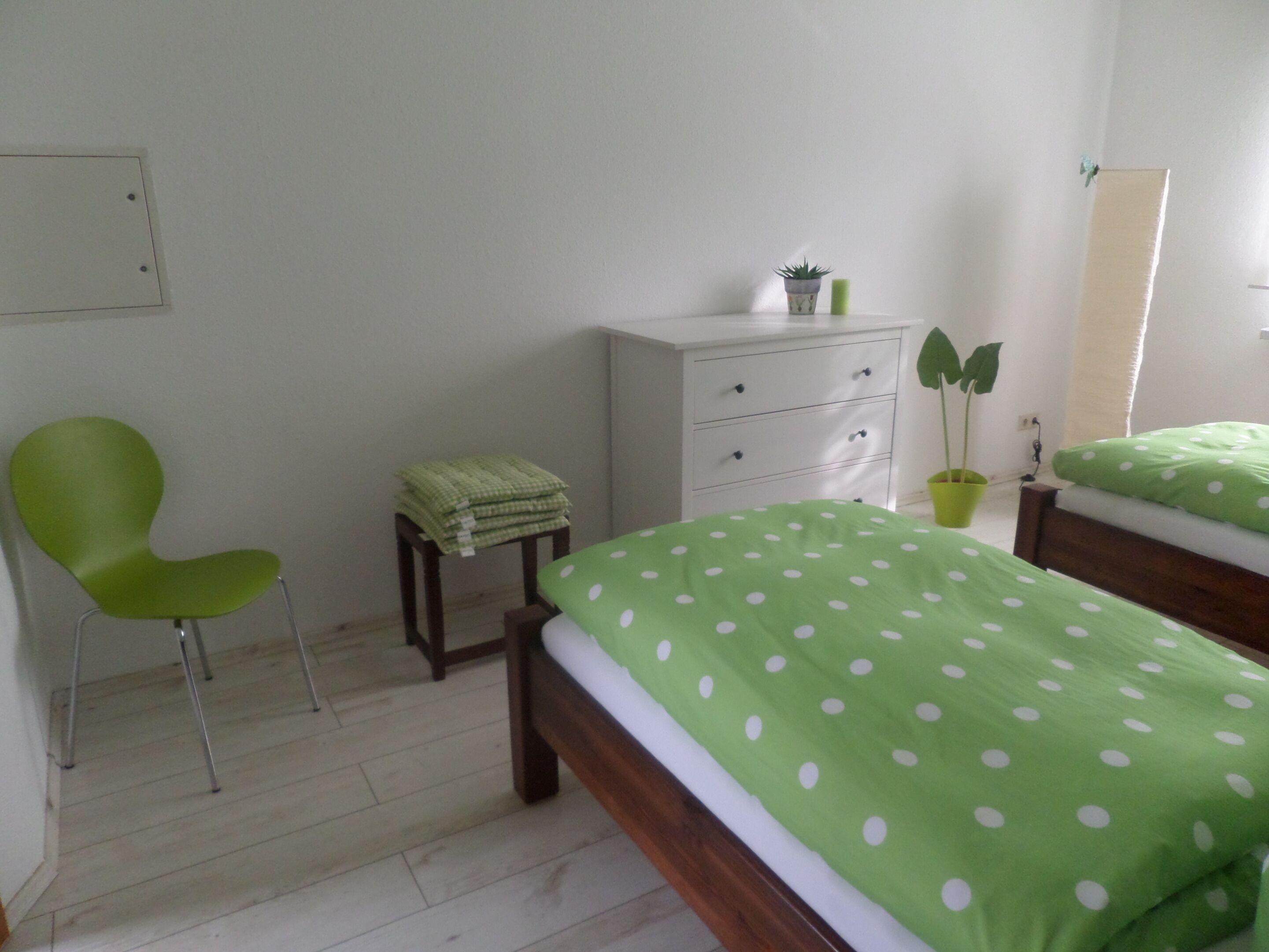 Un dormitorio con una cama, una silla, un aparador y una planta en maceta.