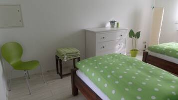 Un dormitorio con una cama, una silla, un aparador y una planta en maceta.