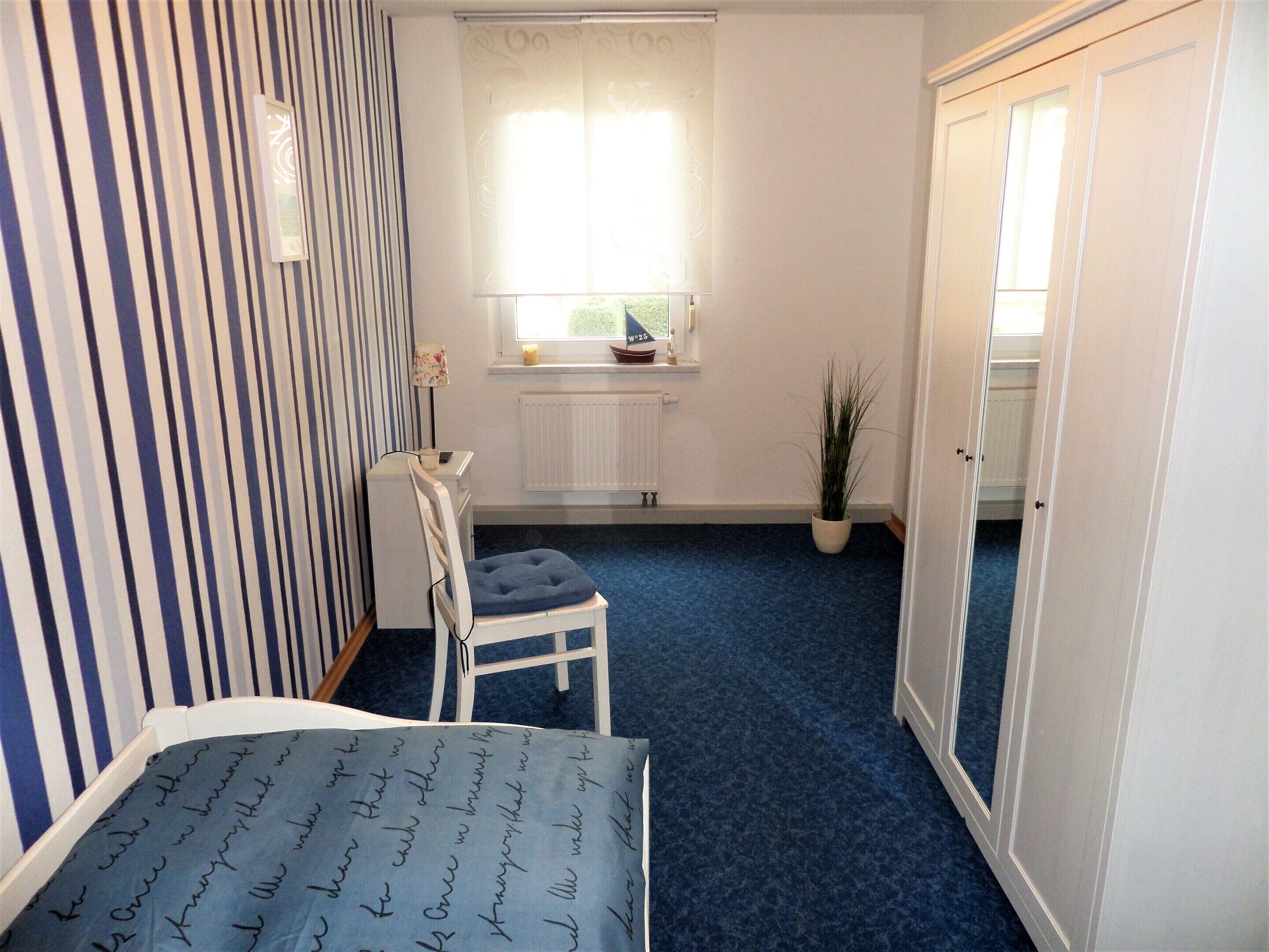 Une chambre avec un mur à rayures, une fenêtre donnant sur un paysage agréable, une chaise, un lit et une armoire.