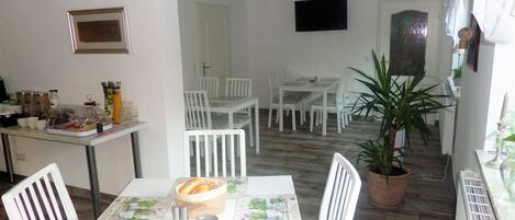 A dining area with white furniture, a table with a floral tablecloth, and a potted plant.
