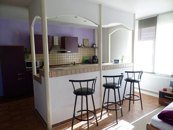 A compact kitchen with a central island, bar stools, and a window with blinds.