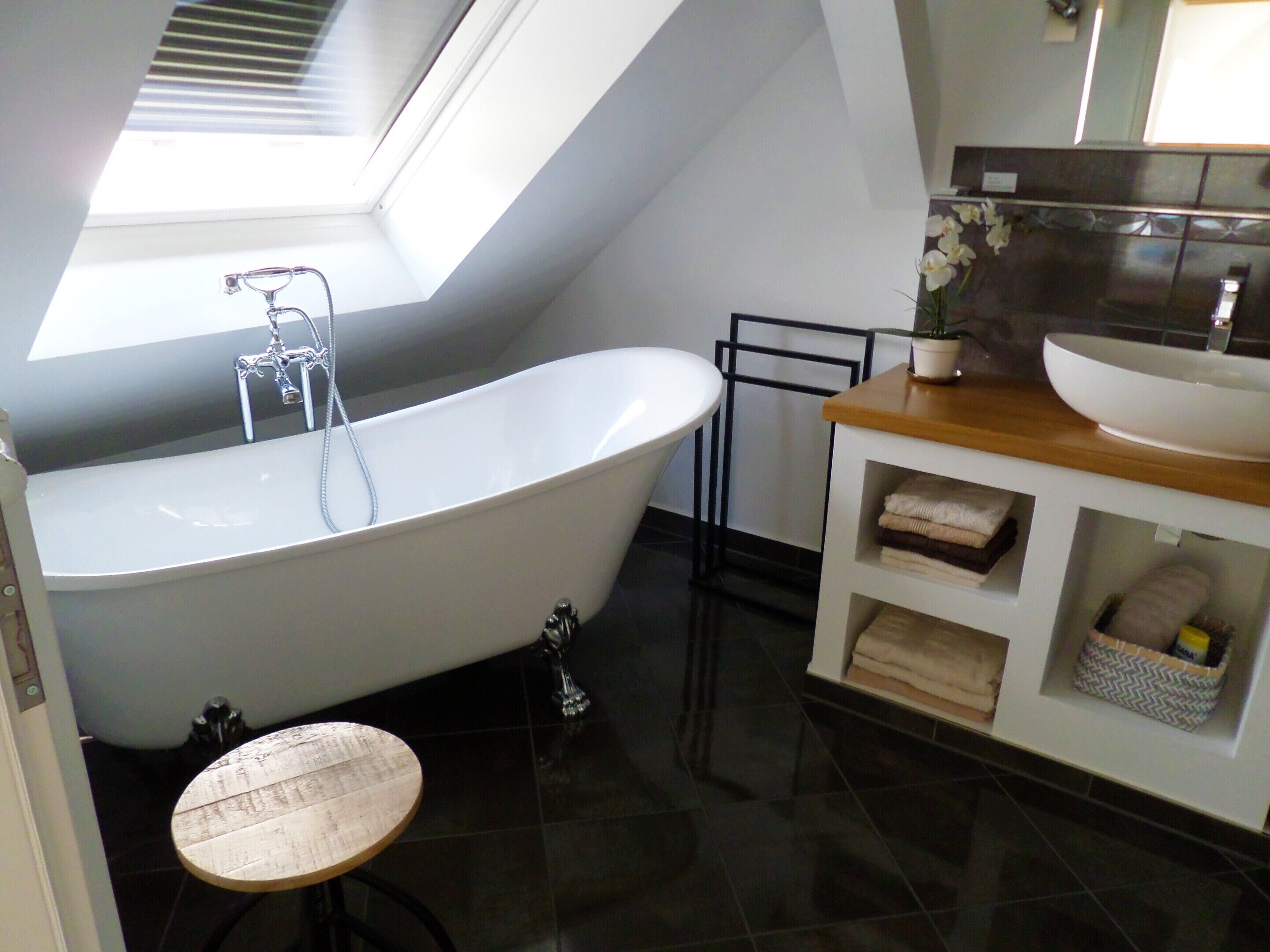 A modern bathroom with a freestanding bathtub, a small round table, a vanity with a sink, and a skylight above the bathtub.