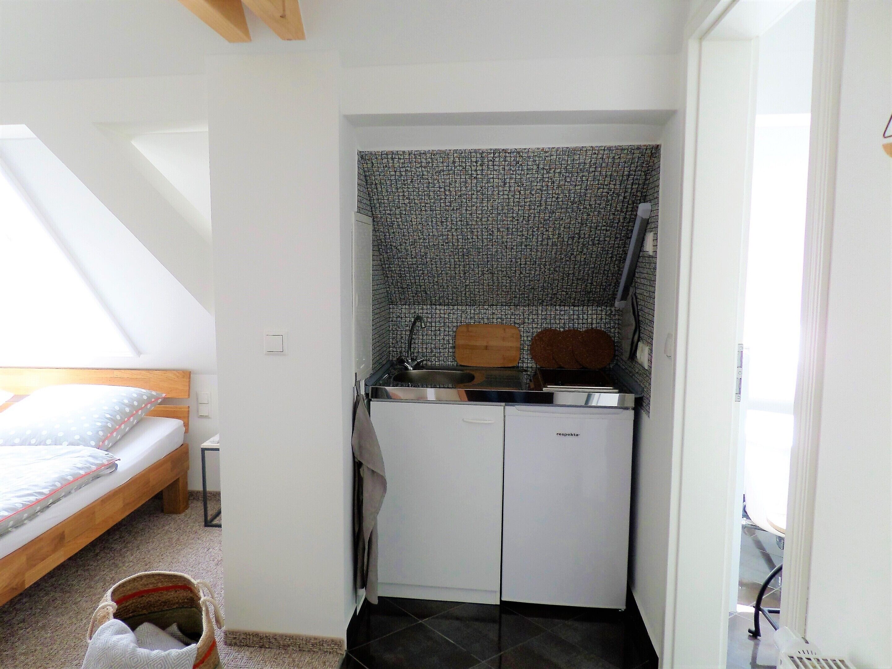 A compact kitchen with a sink, wooden cutting board, and a refrigerator.