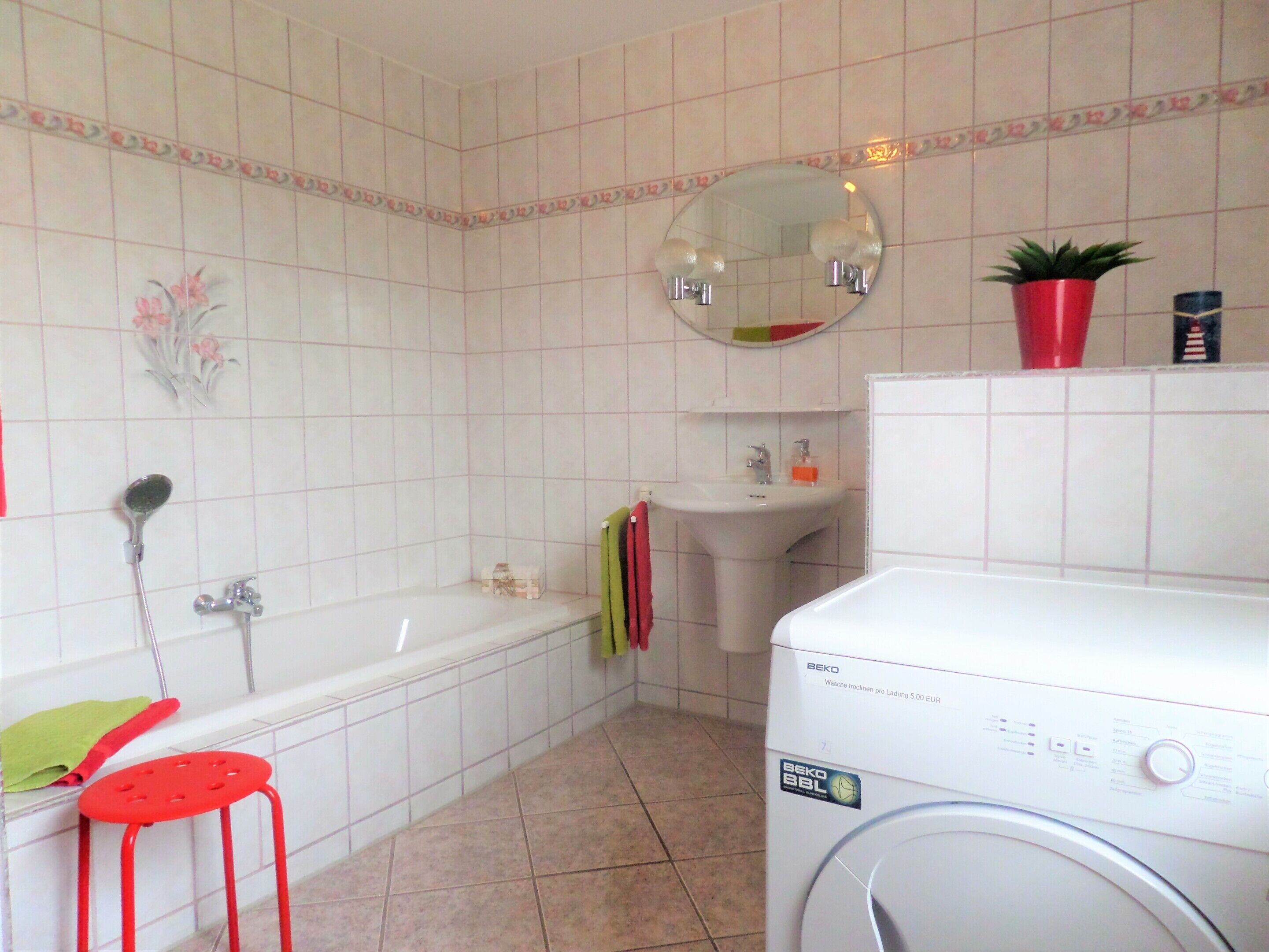Een badkamer met een bad, een wastafel, een spiegel, een rode kruk en een wasmachine.