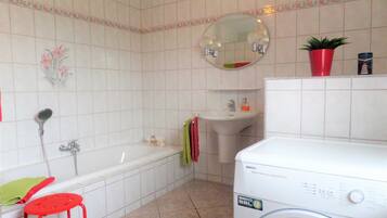 Een badkamer met een bad, een wastafel, een spiegel, een rode kruk en een wasmachine.