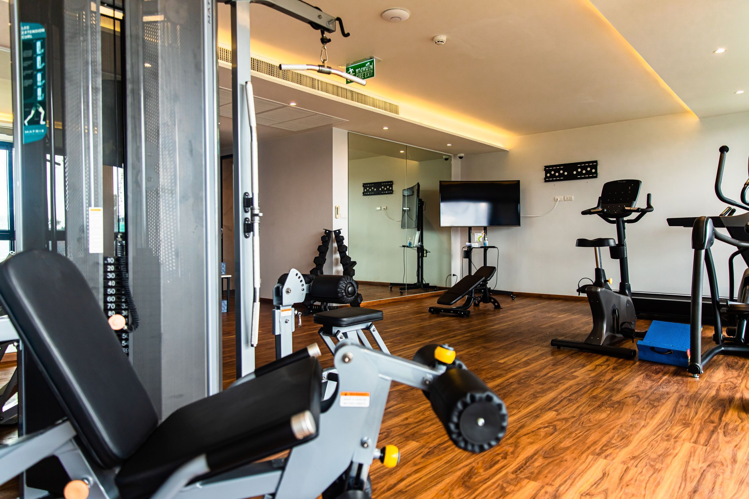 Ein Fitnessraum mit Trainingsgeräten, einem Fernseher und Holzboden.
