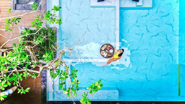 Uma piscina com deck revestido, rodeada por vegetação e um deck de madeira.
