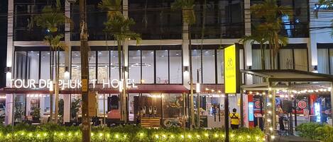 A hotel with a prominent sign, outdoor seating area, and palm trees.