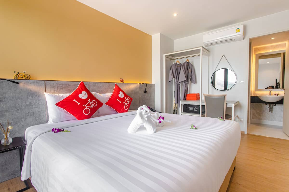 A hotel room with a bed, a desk, a chair, a mirror, and a bathroom.