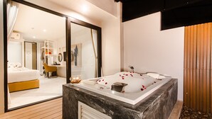 Um banheiro moderno com um espelho grande, uma banheira com pétalas de rosa e piso de madeira.
