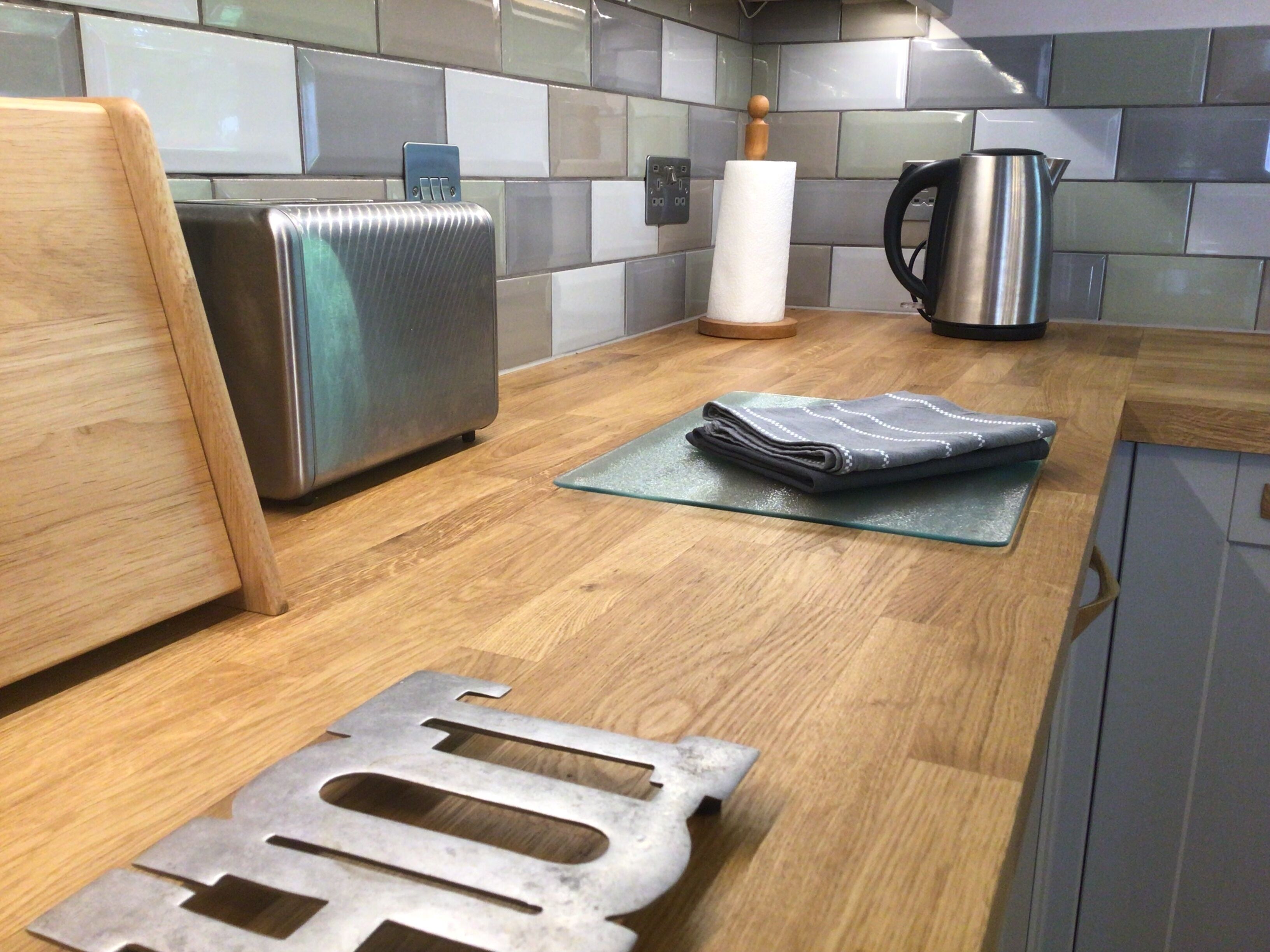 A kitchen with a stainless steel toaster, a kettle, and a folded towel on a glass cutting board.