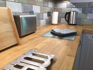 A kitchen with a stainless steel toaster, a kettle, and a folded towel on a glass cutting board.