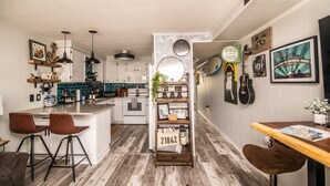 Una cocina moderna con armarios blancos, una isla central con taburetes y un estante de madera con adornos.