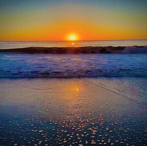 Pôr do sol sobre uma praia com ondas e céu claro.