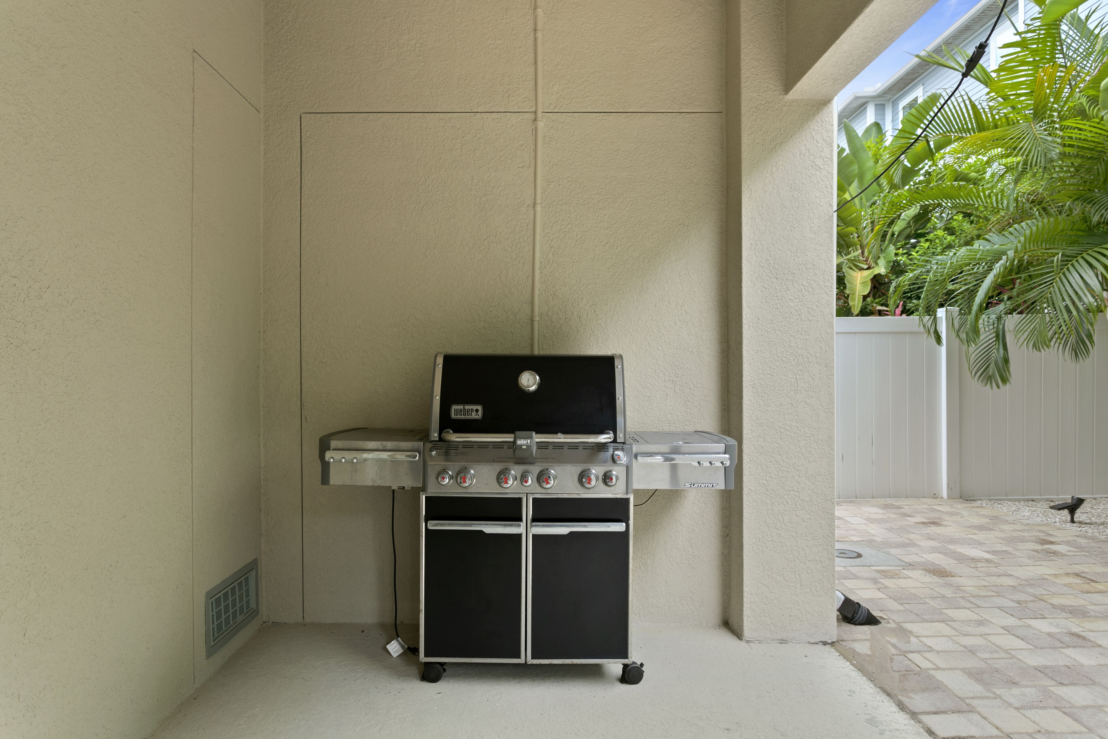 Una griglia Weber con quattro fuochi e un pensile, situata in un'area esterna coperta, dotata di pavimento piastrellato e recinzione bianca.