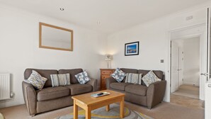 A living room with two sofas, a coffee table, a lamp, and a framed picture on the wall. - Surf Deck - Spectacular Views, Close to Beach (Penally)