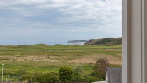 A coastal landscape with grassy fields, a cliff, and a body of water. - Surf Deck - Spectacular Views, Close to Beach (Penally)