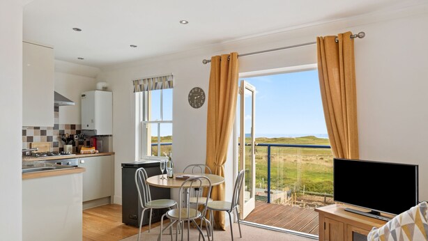 A modern kitchen with a dining area, a TV, and a balcony with a view. - Surf Deck - Spectacular Views, Close to Beach (Penally)