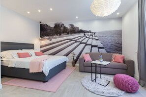 A modern bedroom with a large bed, a sofa, a small table, and a decorative rug. - Unique Studio Apartment (Zadar)