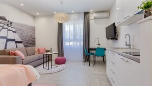 Habitació moderna i ben il·luminada amb sofà, taula petita, cadira, televisió i zona de cuina.