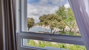 Vista des d'una finestra amb cortines, que mostra un cos d'aigua, arbres i una riba llunyana.