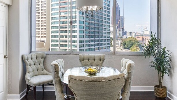 A dining area with a round table and four chairs, a hanging light fixture, and a view of tall buildings through large windows. - 1001 Walk to Soccer 2026, MBS, DT ATL, Parking (Atlanta)