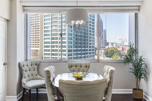 A dining area with a round table and four chairs, a hanging light fixture, and a view of tall buildings through large windows. - 1001 Walk to Soccer 2026, MBS, DT ATL, Parking (Atlanta)