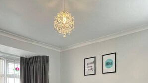 Quarto com cama, mesas de cabeceira, escrivaninha e janela com cortinas.
