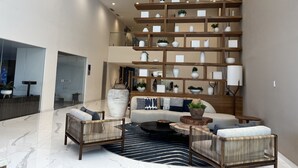 A spacious lobby with a high ceiling, a central seating area with sofas and chairs, and a large, multi-tiered wooden shelving unit displaying various decorative items. - Increible depa con vista al mar. Z.dorada(factura) (Mazatlán)