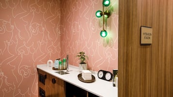 A bathroom with a pink patterned wall, a white countertop, a sink, a mirror, a clock, and a sign reading "HYDRATION STATION".