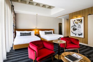 A hotel room with two beds, a red armchair, a small round table with a book and a glass of wine, and a large abstract painting on the wall. - Hotel Indy, Indianapolis, a Tribute Portfolio Hotel (Indianapolis)