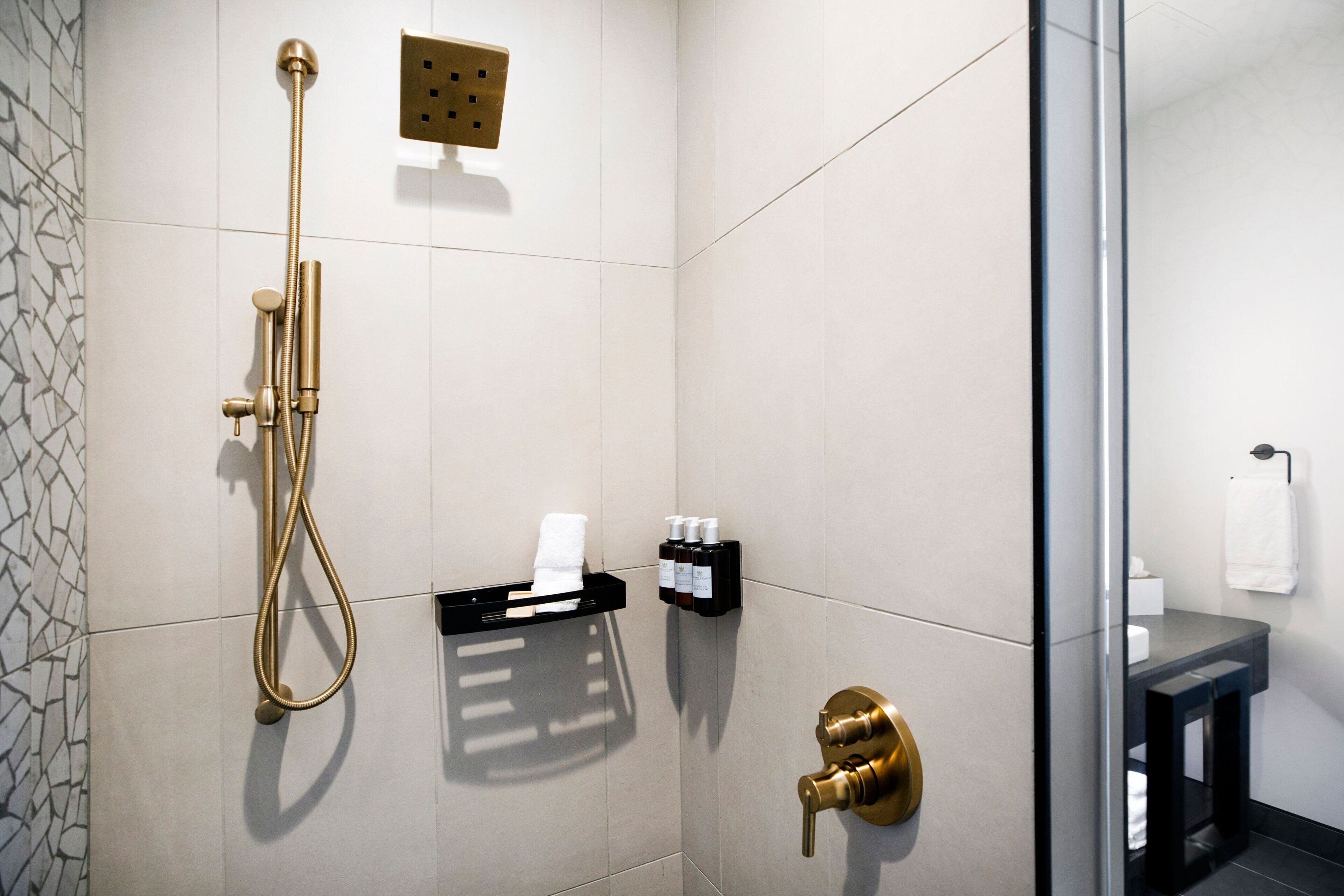 A modern bathroom with a shower, a towel rack, and a soap dispenser.