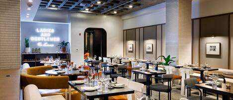A modern restaurant with tables set for dining, a neon sign on the wall, and a mix of seating options including booths and chairs.