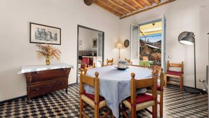 Ein Essbereich mit Schachbrettboden, Holzstühlen, einem runden Tisch mit Tischdecke, einer Holzkommode und einem gerahmten Bild an der Wand.