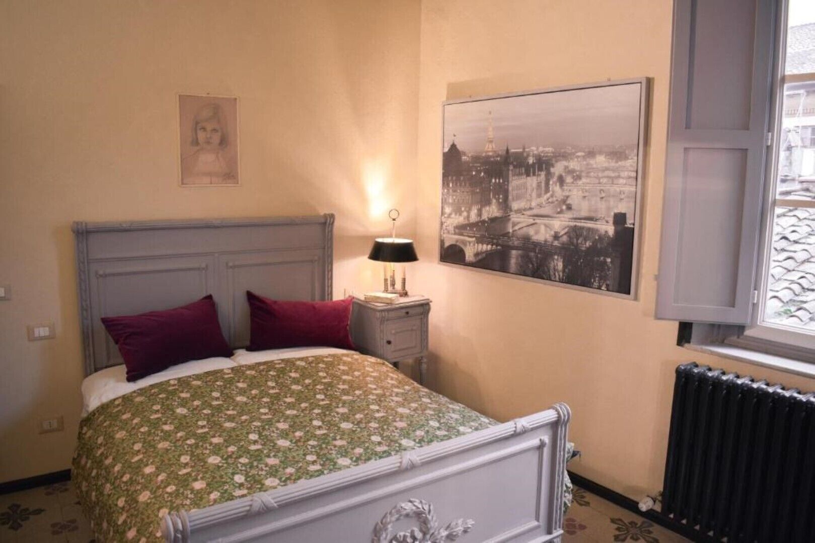 Une chambre à coucher avec un lit, deux oreillers, une table de chevet, une lampe, un tableau encadré au mur et une fenêtre donnant sur un pont.