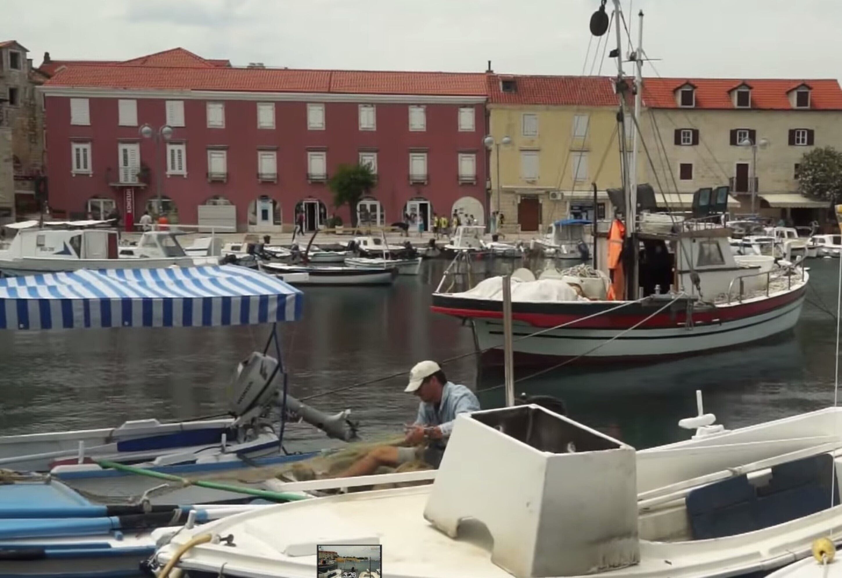 Un puerto deportivo con barcos amarrados, un hombre en una embarcación y edificios al fondo.