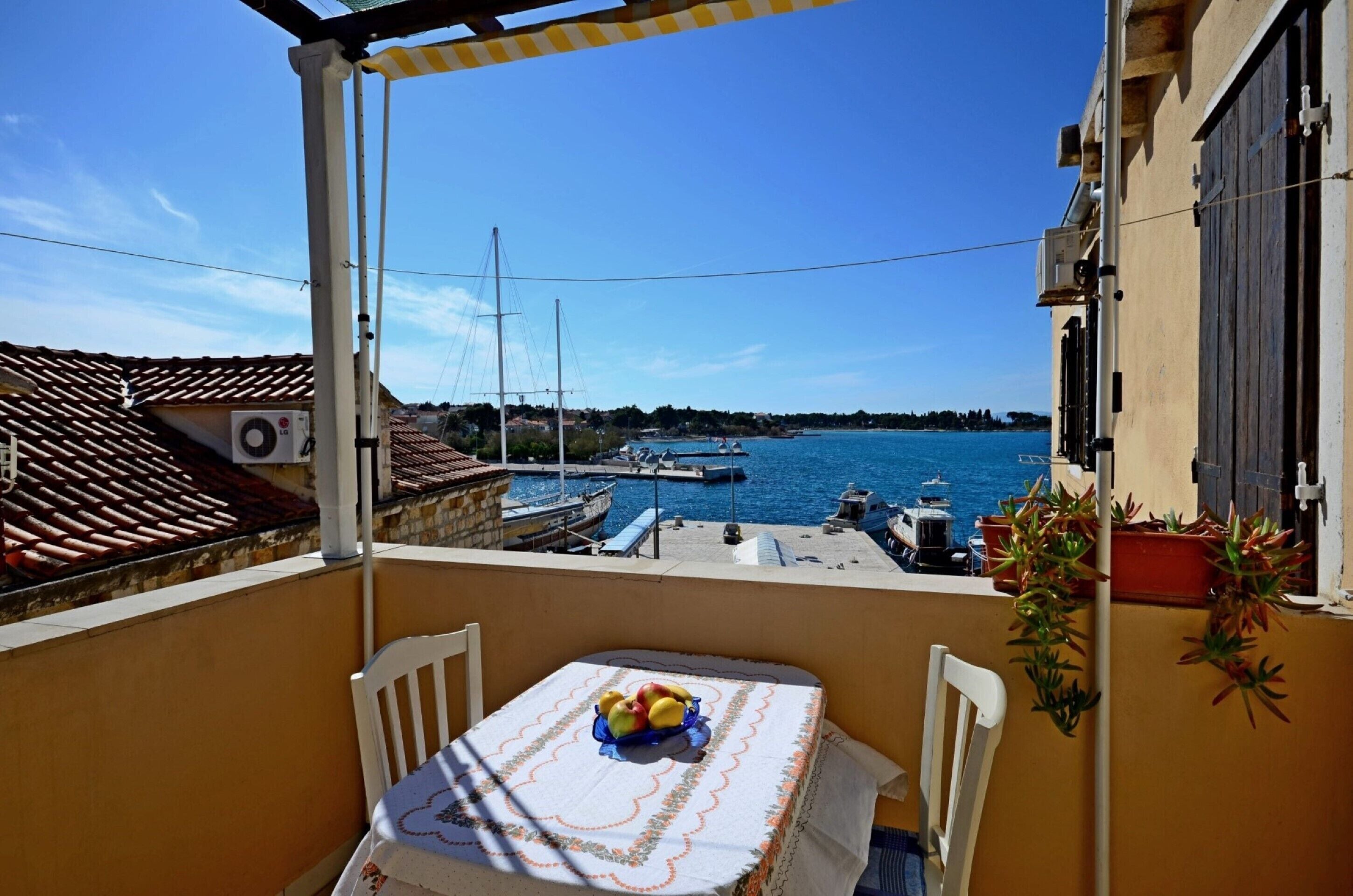 A balcony with a table set for two, overlooking a marina with boats and a clear blue sky.