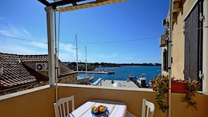 Varanda com mesa posta para dois, vista para uma marina com barcos e céu azul límpido.