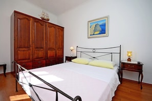 A bedroom with a large wooden wardrobe, a bed with a metal frame, two bedside tables with lamps, and a painting on the wall. - A1 - apt With Terrace, Best Location in Supetar (Supetar)