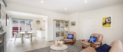 A spacious living room with a beige sofa, two armchairs, a coffee table, and a bookshelf.