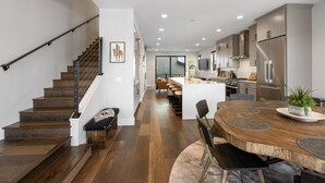 A modern kitchen with a central island, wooden flooring, and a staircase with a black railing.
