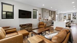A spacious living room with leather sofas, a coffee table, and a TV mounted on the wall.